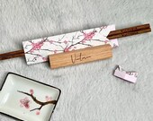 A personalized Japanese-inspired chopstick set featuring custom-engraved wooden chopsticks with an elegant wooden name stand, cherry blossom origami wrap, matching origami chopstick rest, and a ceramic soy sauce dish with a cherry blossom design. thumbnail 1