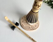 Personalized matcha tea set featuring engraved bamboo whisk and scoop with rhinestones, ceramic black whisk holder, scoop rest, and double-sided engraved wooden coaster. One side of the coaster shows Japanese matcha characters, the other features mat thumbnail 4