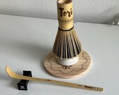 Personalized matcha tea set featuring engraved bamboo whisk and scoop with rhinestones, ceramic black whisk holder, scoop rest, and double-sided engraved wooden coaster. One side of the coaster shows Japanese matcha characters, the other features mat thumbnail 9