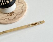 Personalized matcha tea set featuring engraved bamboo whisk and scoop with rhinestones, ceramic black whisk holder, scoop rest, and double-sided engraved wooden coaster. One side of the coaster shows Japanese matcha characters, the other features mat thumbnail 5