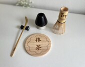 Personalized matcha tea set featuring engraved bamboo whisk and scoop with rhinestones, ceramic black whisk holder, scoop rest, and double-sided engraved wooden coaster. One side of the coaster shows Japanese matcha characters, the other features mat thumbnail 10
